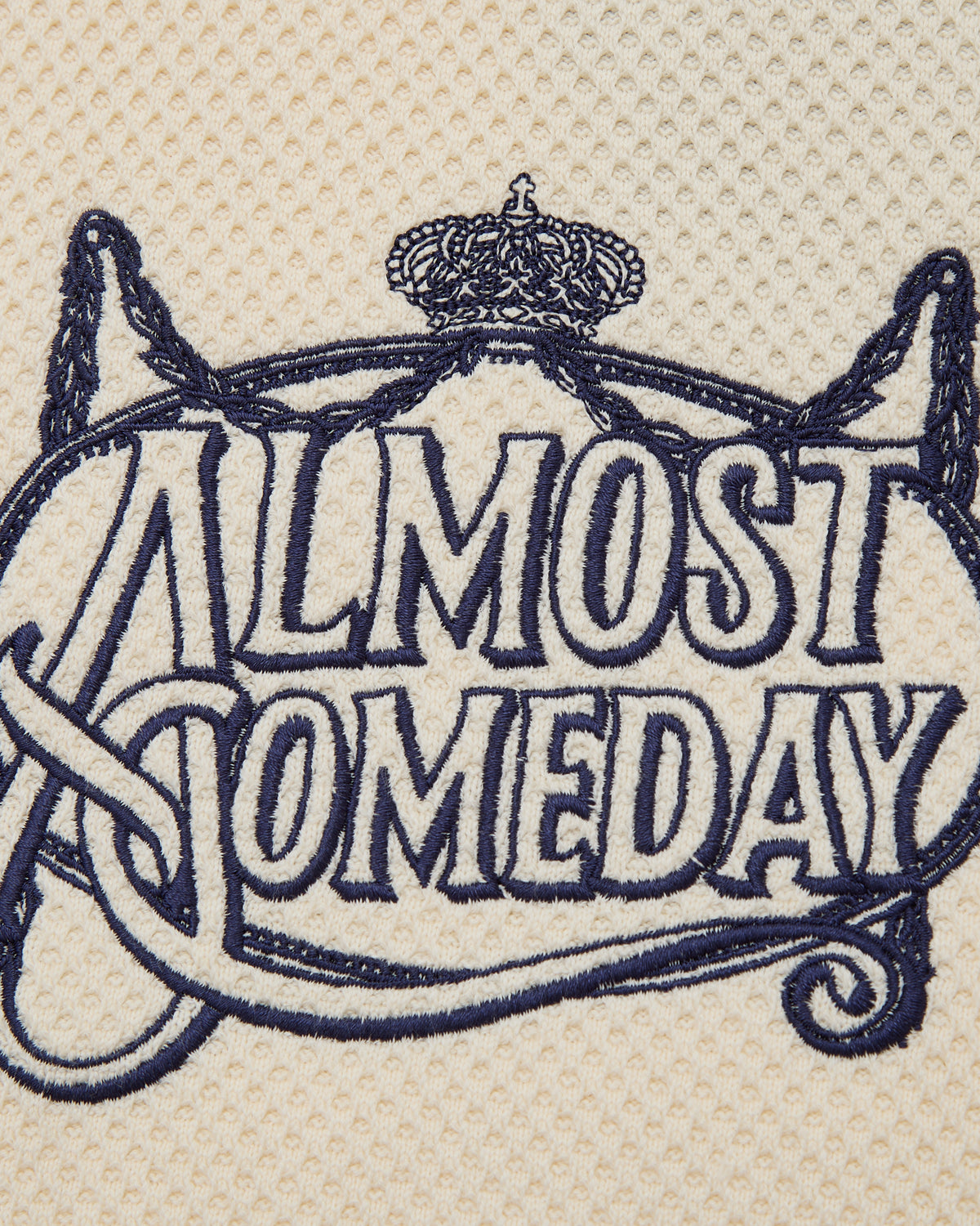Embroidered text 'ALMOST SOMEDAY' with decorative elements on a beige background