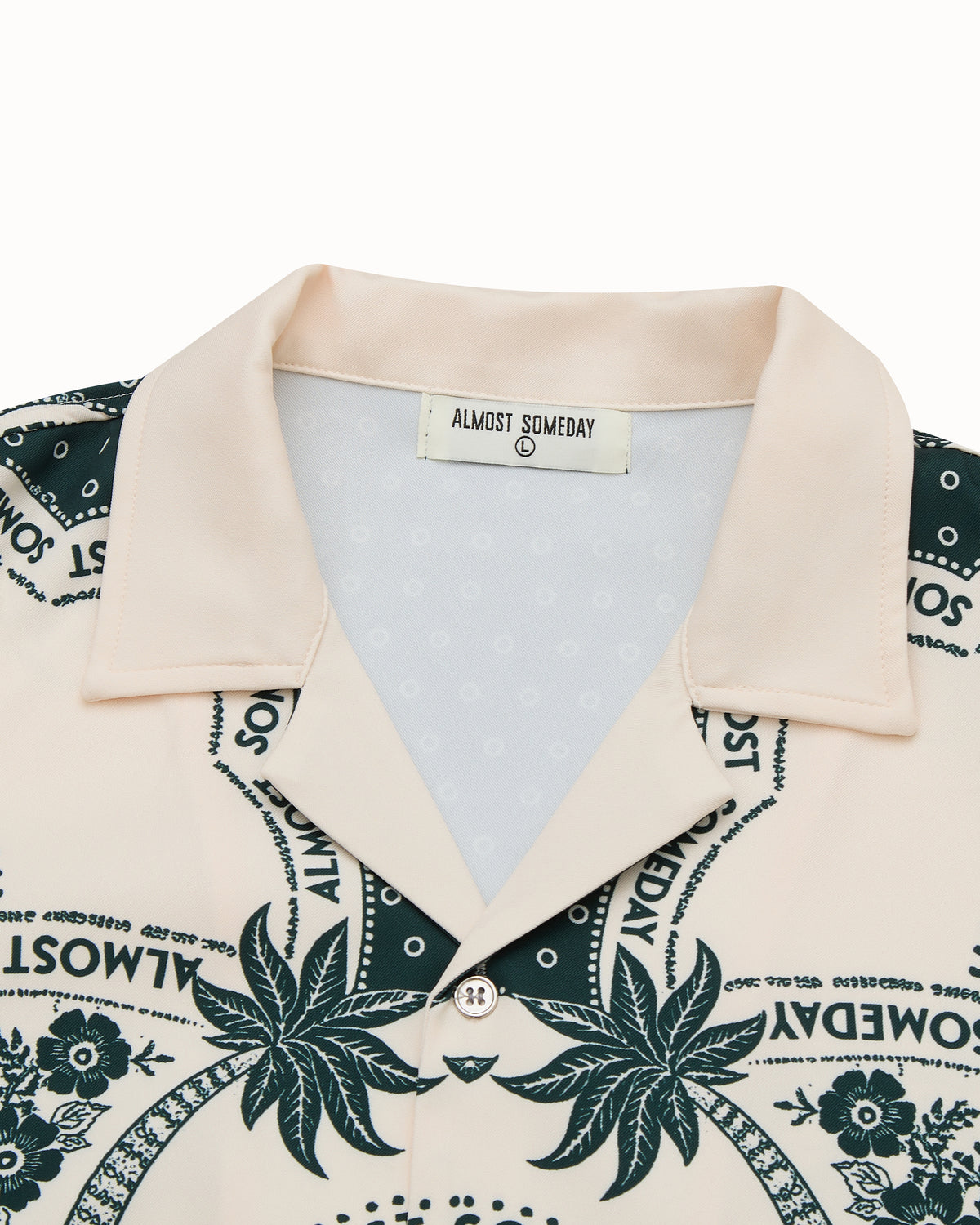 Beige shirt with green floral and text pattern, brand label visible
