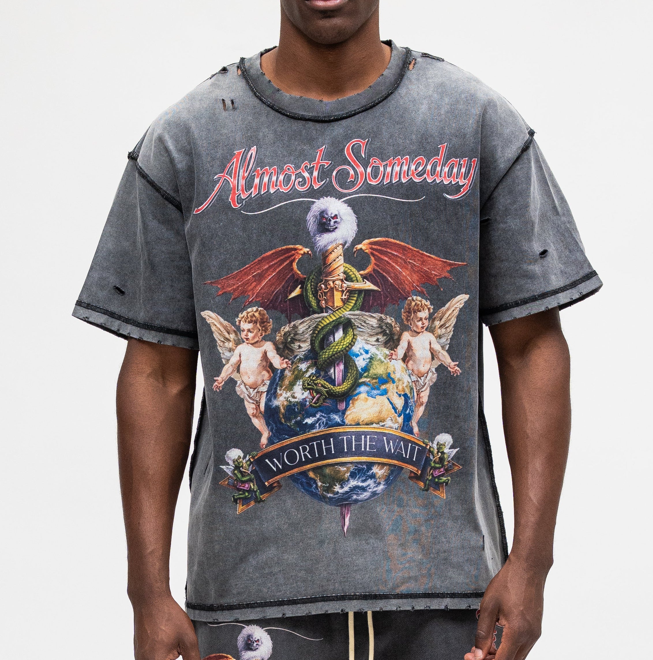 A man modeling a distressed gray graphic t-shirt with a 'Almost Someday' design, paired with matching gray sweatpants, against a plain light gray background.
