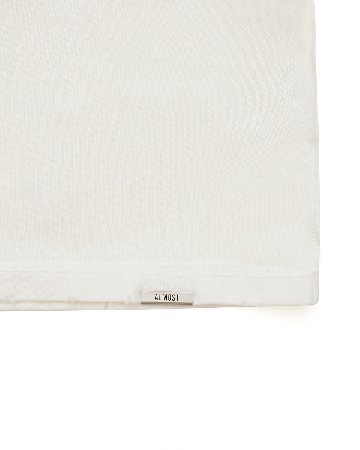 Cream tshirt with a small rectangular object labeled 'ALMOST' on a white background