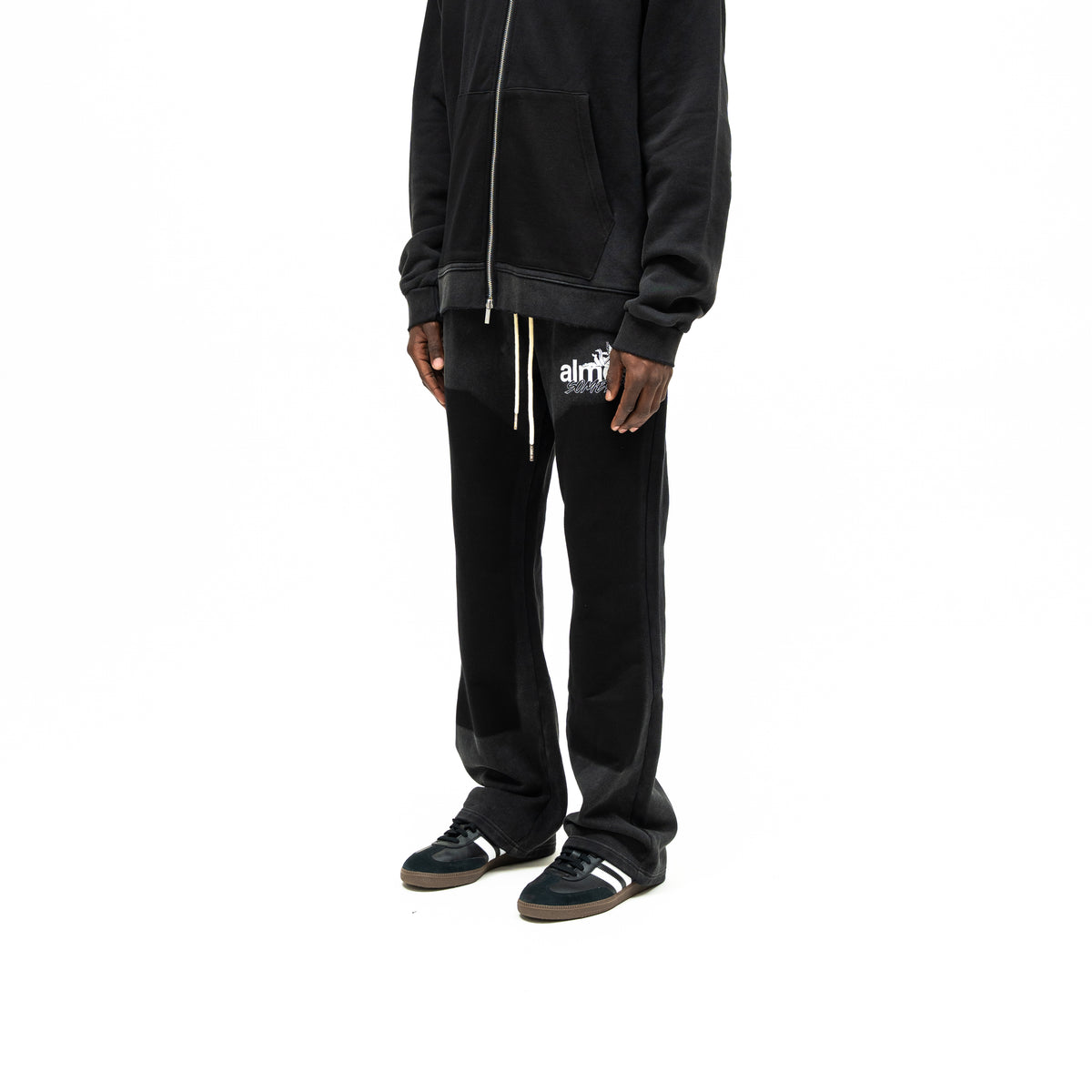 Enemies Flare Bottoms – Black – Three-quarter front view on model styled with a black zip hoodie, showing thigh logo and flared hems