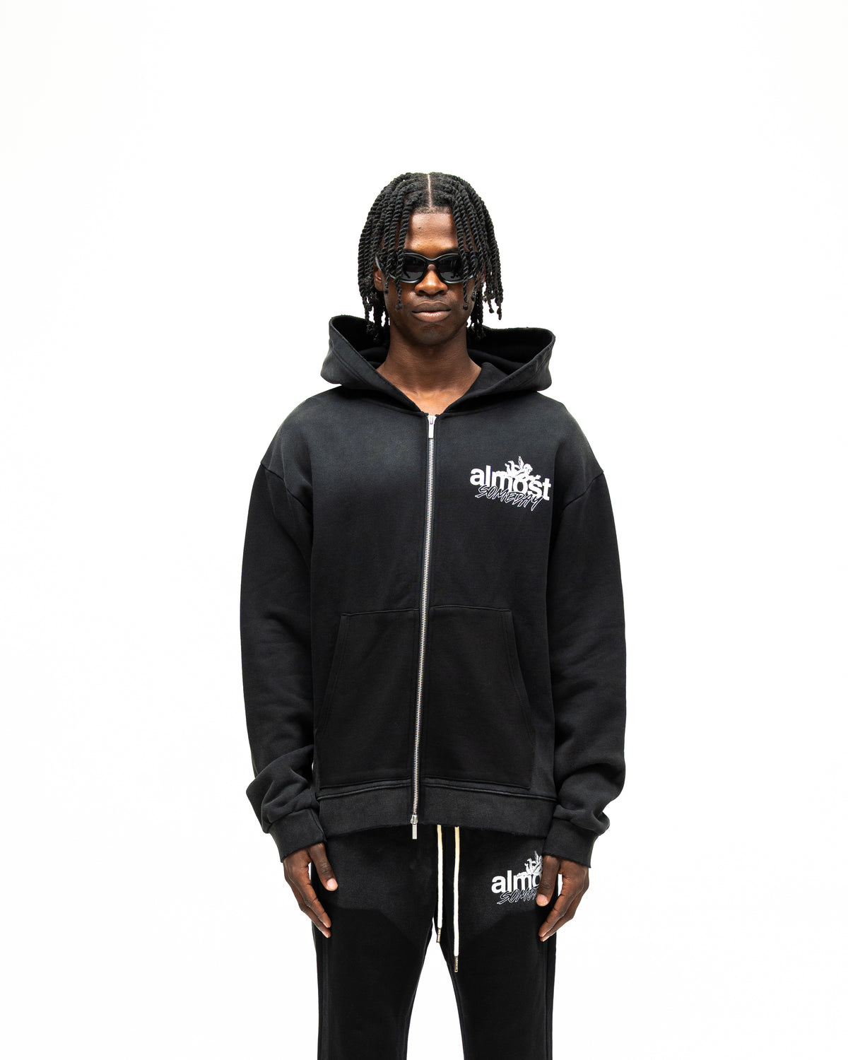 Enemies Zip Hoodie – Black – Front view on model showing full zipper, white chest logo, hood, and front pocket detail