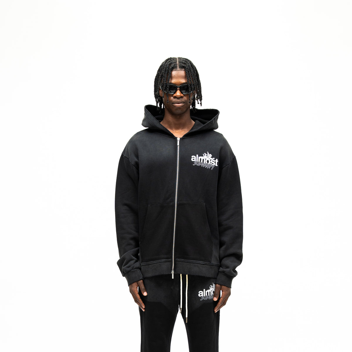 Enemies Zip Hoodie – Black – Front view on model showing full zipper, white chest logo, hood, and front pocket detail