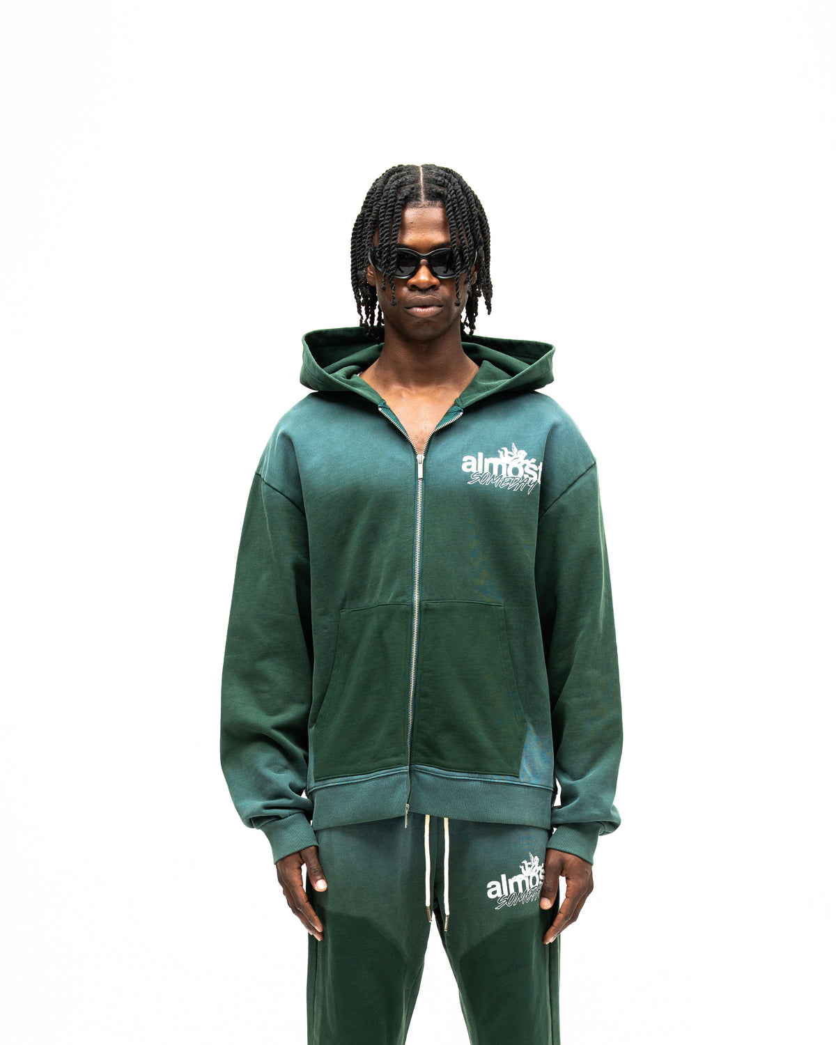 Enemies Zip Hoodie – Green – Front view on model showing full zipper, white chest logo, hood, and dark green front pockets