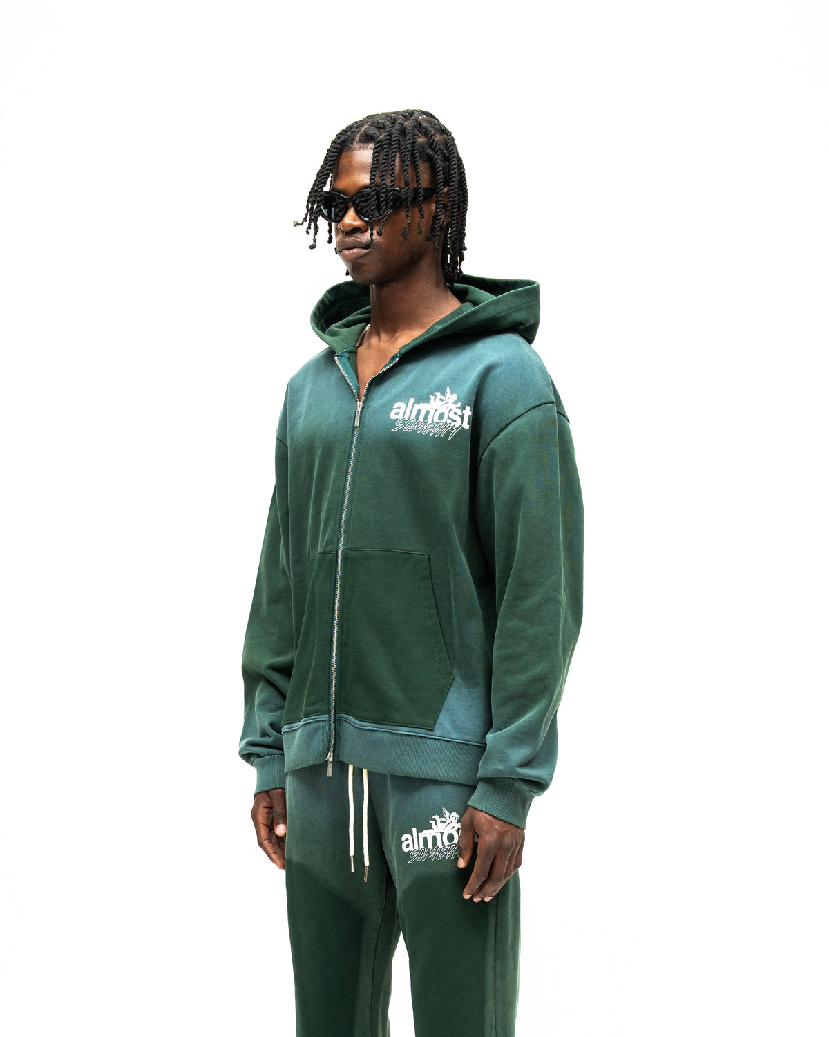 Enemies Zip Hoodie – Green – Three-quarter front view on model showing chest logo, dropped shoulders, and contrasting front pockets