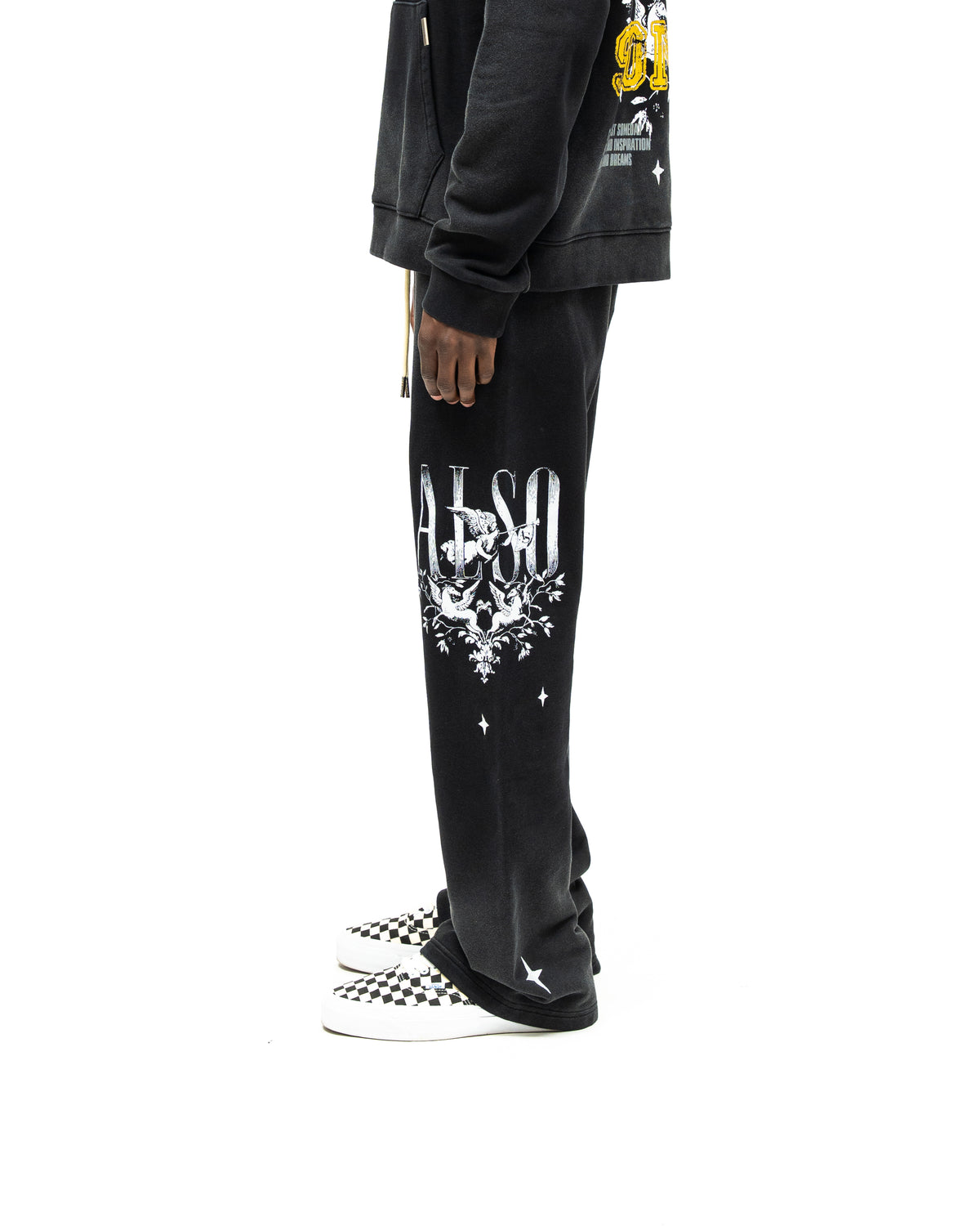 League Flare Sweatpants – Black – Side view on model styled with a hoodie, showing flared sweatpants with white lettering, winged figures, and stars