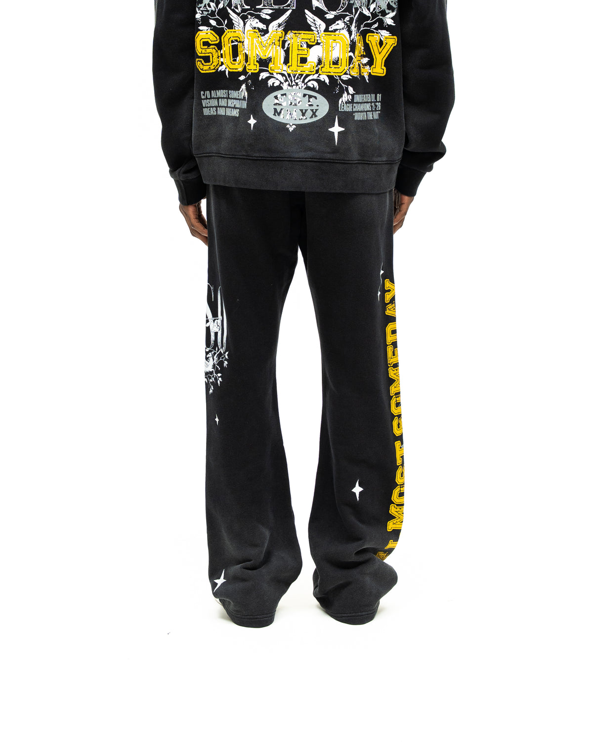 League Flare Sweatpants – Black – Back view on model styled with a hoodie, showing flared sweatpants with yellow side lettering