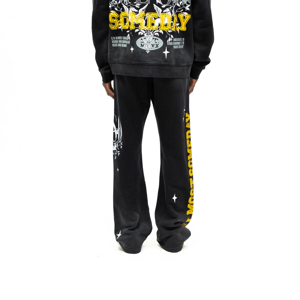 League Flare Sweatpants – Black – Back view on model styled with a hoodie, showing flared sweatpants with yellow side lettering