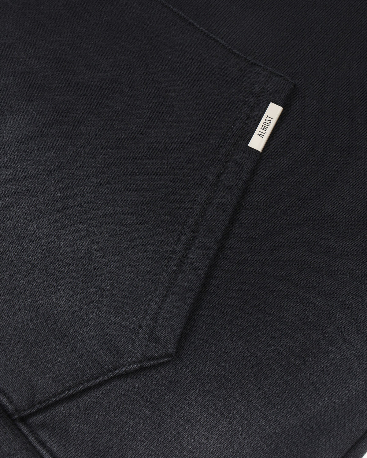 League Hoodie – Black – Close-up of kangaroo pocket with metal ALMOST logo tab