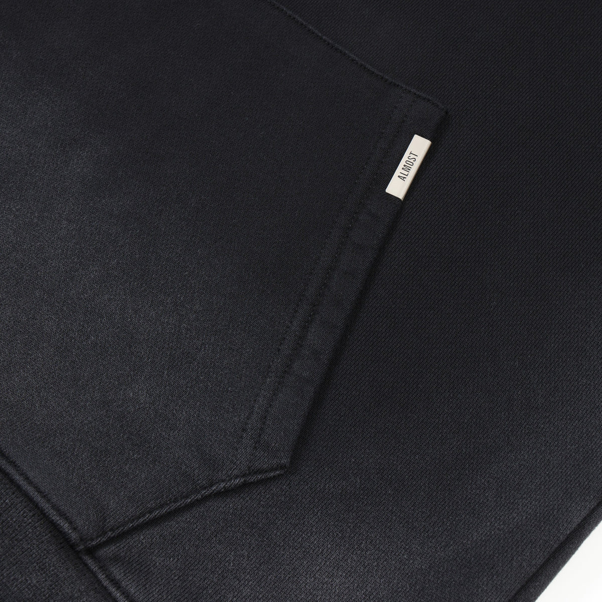 League Hoodie – Black – Close-up of kangaroo pocket with metal ALMOST logo tab