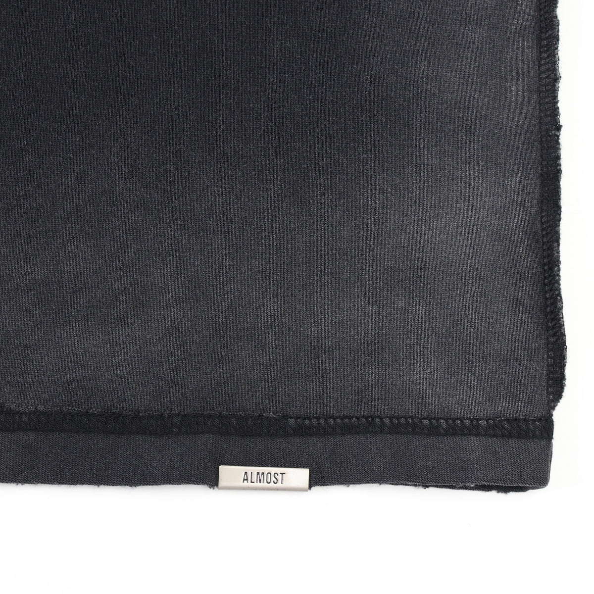 League Tee – Black – Close-up of bottom hem with metal ALMOST logo tab