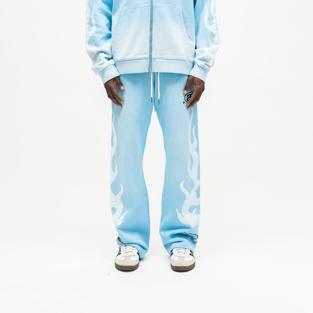 Members Flare Sweatpants – Light Blue – Front view on model showing cream drawstrings, black thigh logo, white leg flames, and flared hems