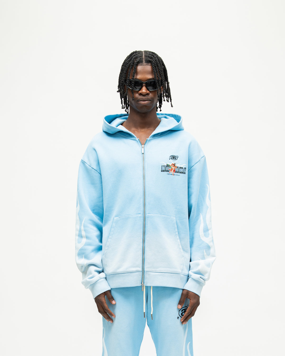 Members Zip Hoodie – Light Blue – Front view on model showing zip closure, chest graphic, front pockets, and white sleeve flames