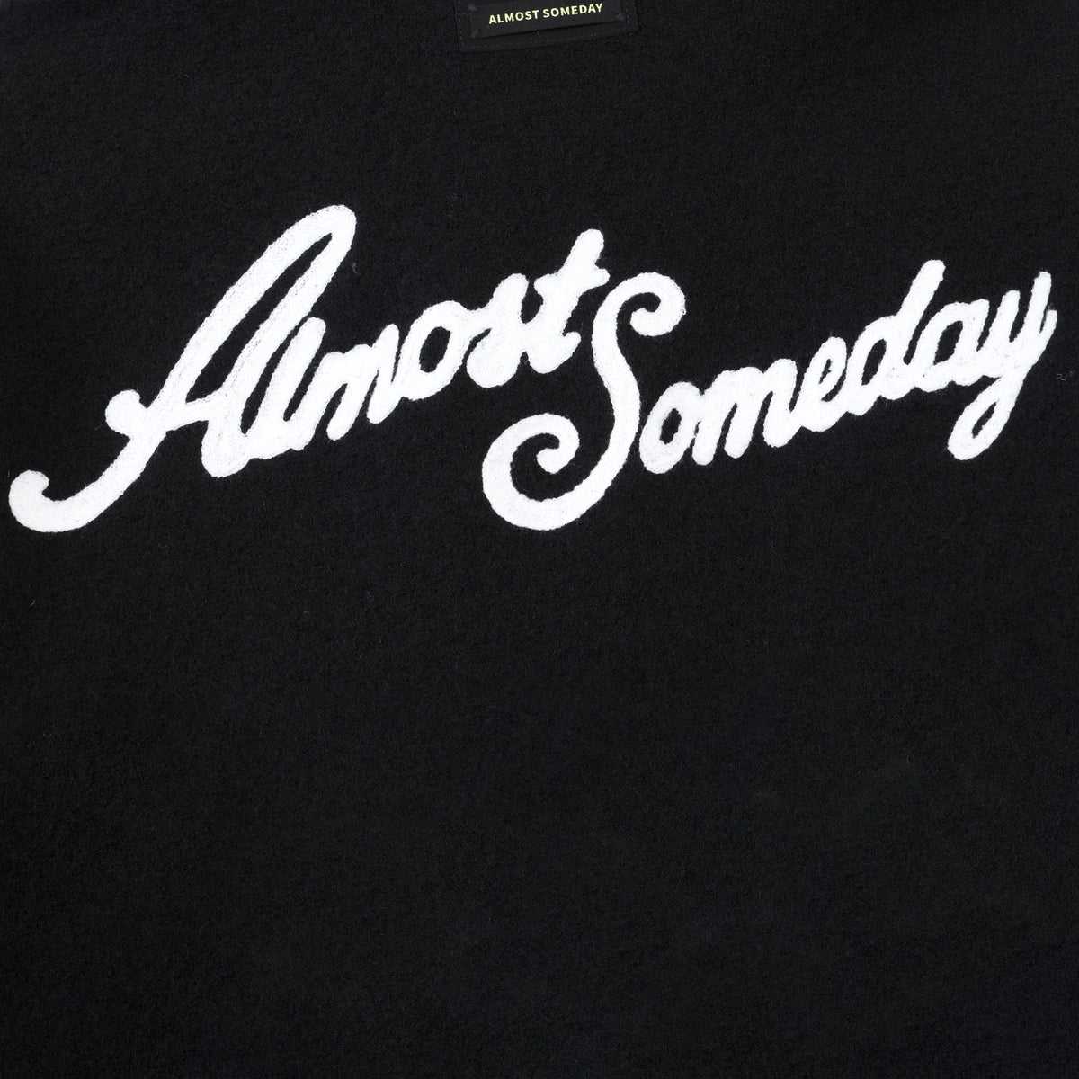 Saint Cropped Wool Jacket – Black – Close-up of white back script and black brand patch
