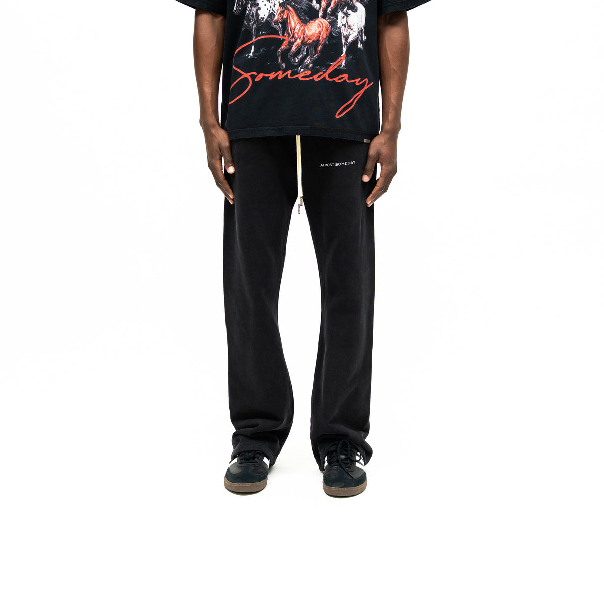 Smoke Flare Bottoms – Black – Front view on model styled with graphic tee, showing cream drawstrings, white thigh logo, and flared hems