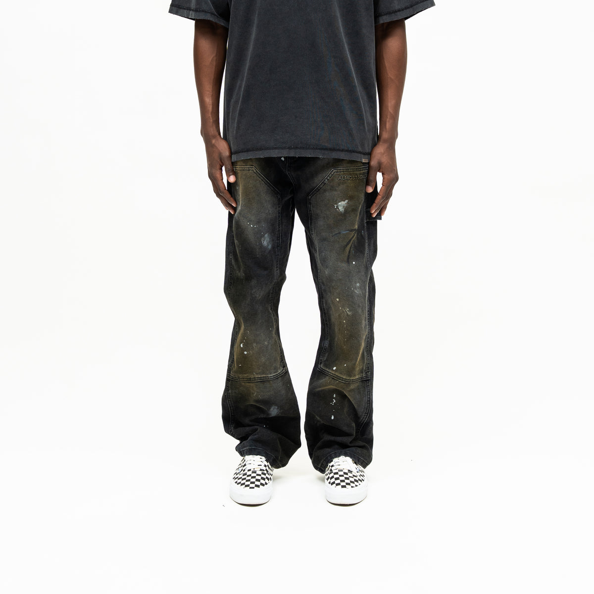 Spade Pants – Black – Front view on model styled with washed tee, showing faded thigh panels, white paint splatters, and wide hems