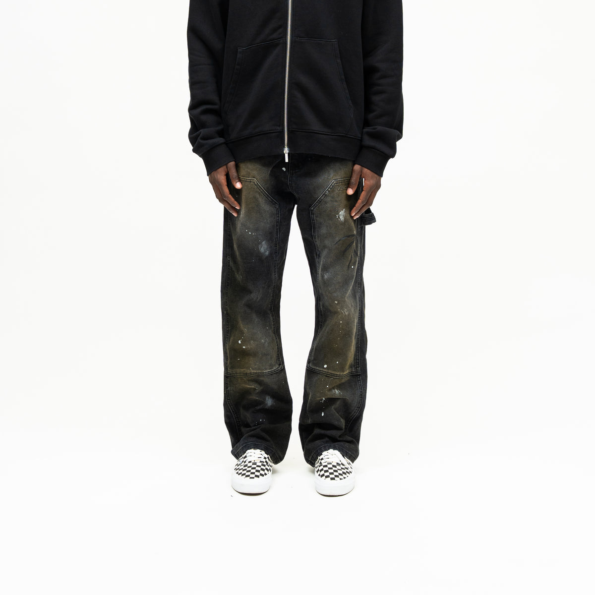 Spade Pants – Black – Front view on model styled with black zip hoodie, showing faded panels and white paint splatters