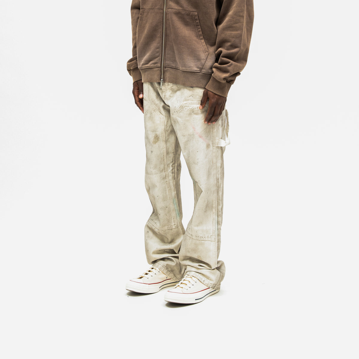 Spade Pants – Cream – Three-quarter front view on model styled with brown zip hoodie, showing thigh panels and utility loop