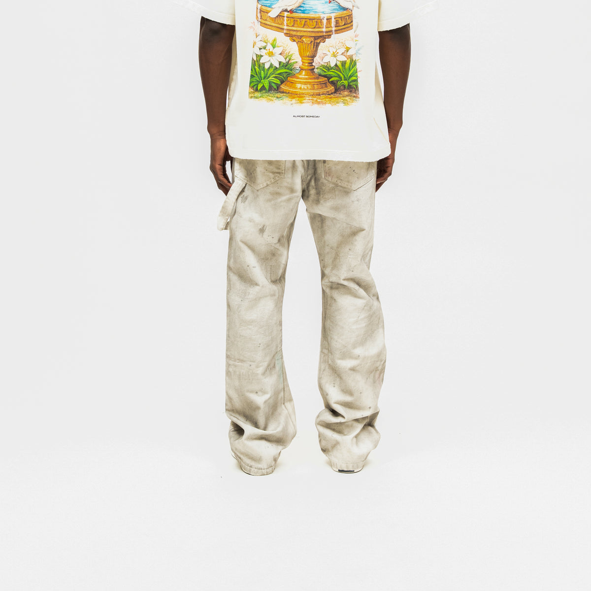 Spade Pants – Cream – Back view on model styled with white graphic tee, showing rear pockets, utility loop, and mottled finish