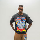 A man modeling a washed black graphic t-shirt with a colorful 'ALMOST SOMEDAY' band logo and skeleton/rose design, paired with brown drawstring shorts against a plain light gray background.