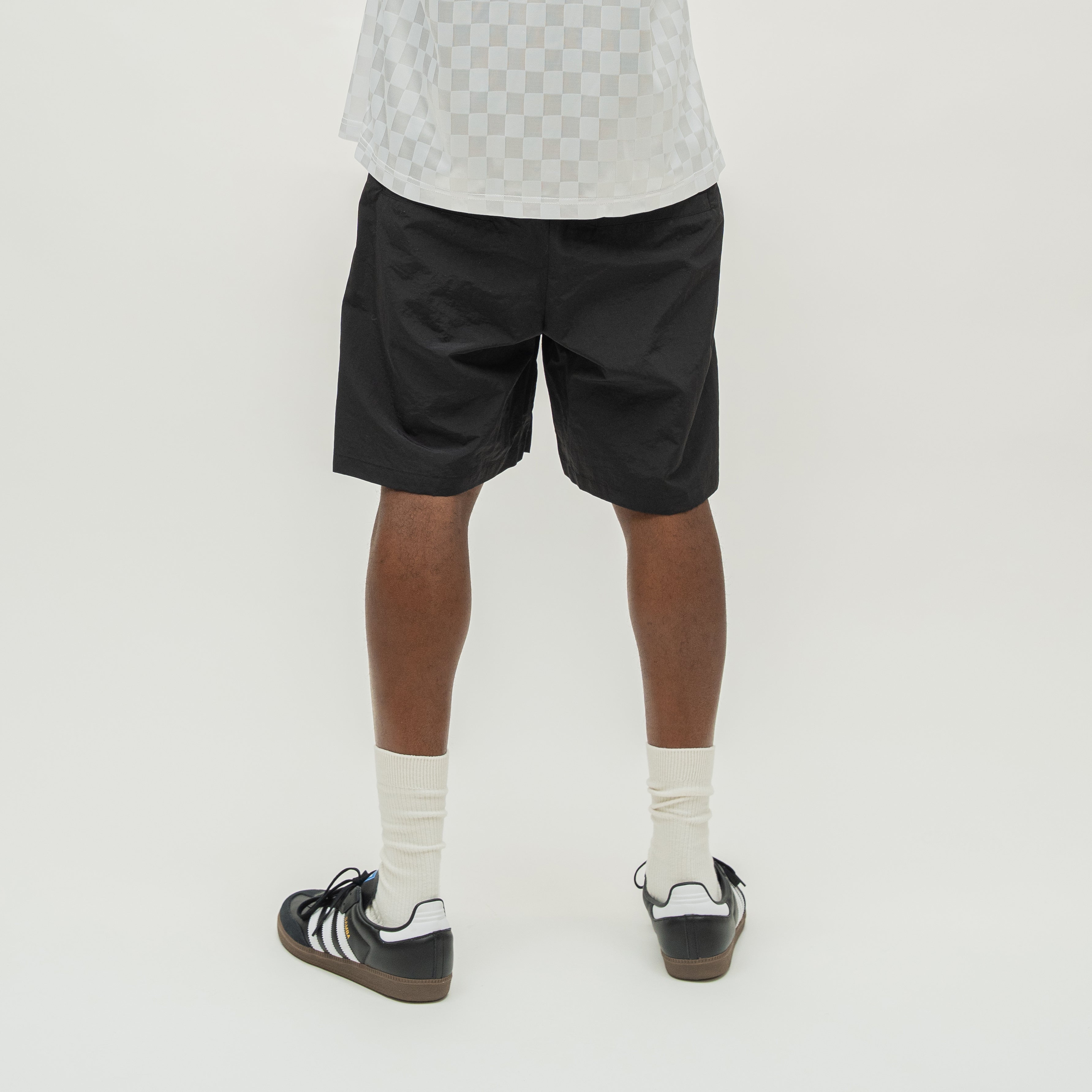 A person shown from the back wearing black athletic shorts, white crew socks, and black-and-white sneakers against a plain light gray studio background.
