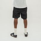 A person shown from the back wearing black athletic shorts, white crew socks, and black-and-white sneakers against a plain light gray studio background.