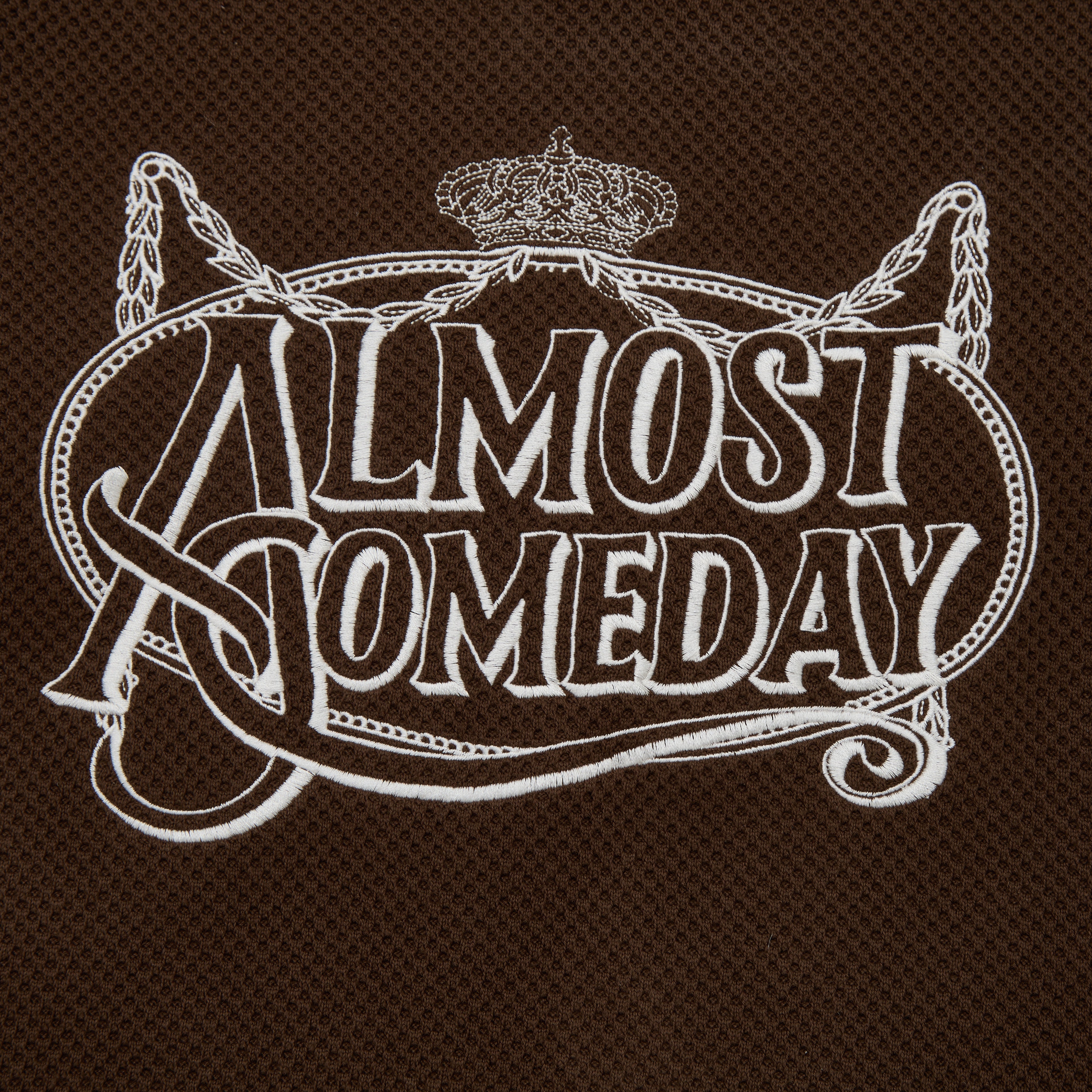 Embroidered text 'Almost Someday' on a brown textured background