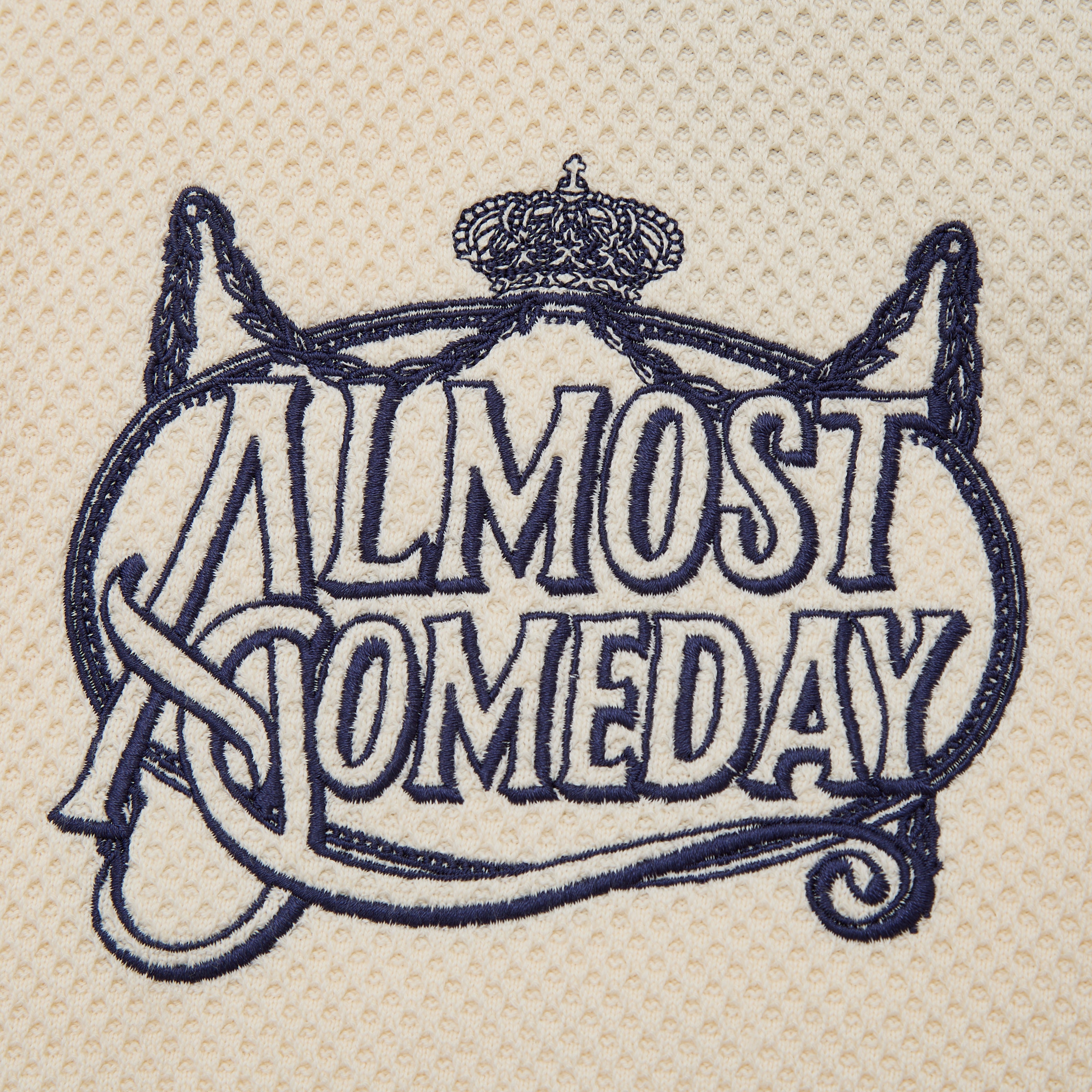 Embroidered text 'ALMOST SOMEDAY' with decorative elements on a beige background