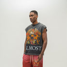 A man modeling a sleeveless black t-shirt with a large orange and gold eagle graphic and the word 'ALMOST' printed on the front, paired with red sweatpants against a plain light gray background.