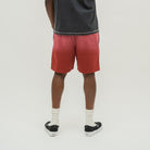 A person shown from the back wearing red gradient tie-dye shorts, a dark gray t-shirt, white socks, and black slip-on sneakers against a light gray studio background.