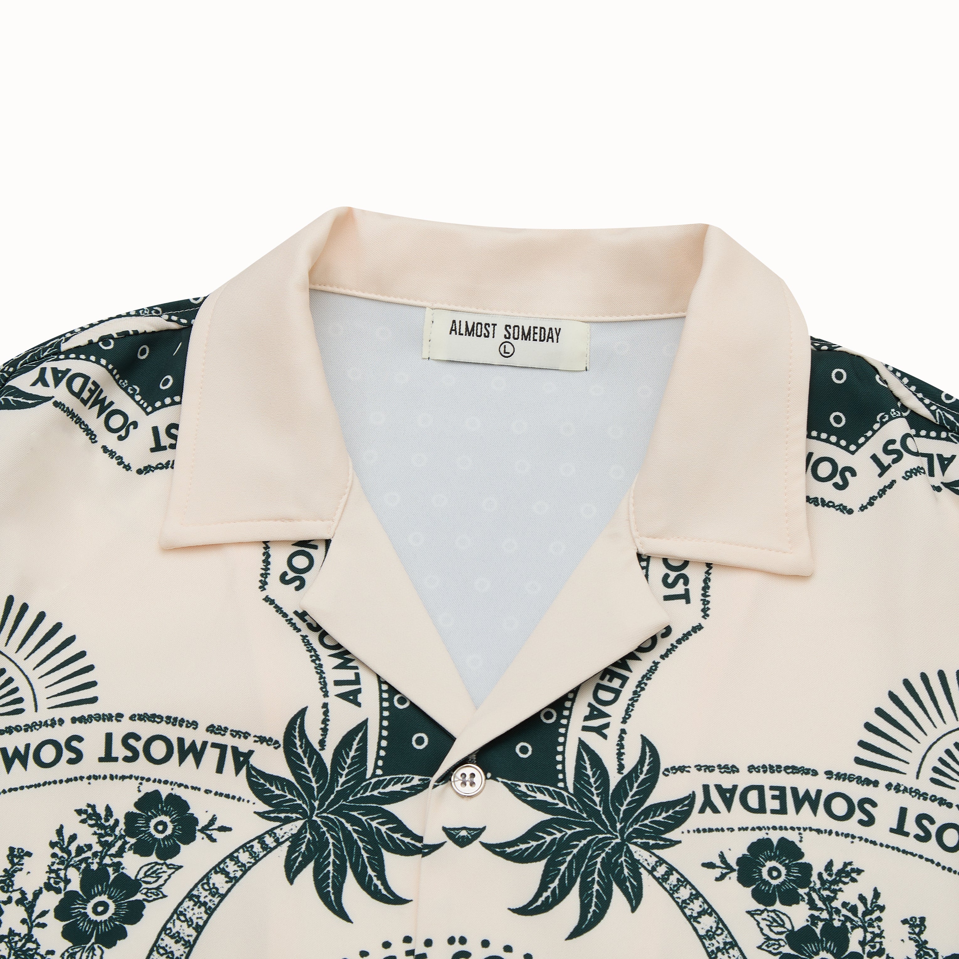 Beige shirt with green floral and text pattern, brand label visible