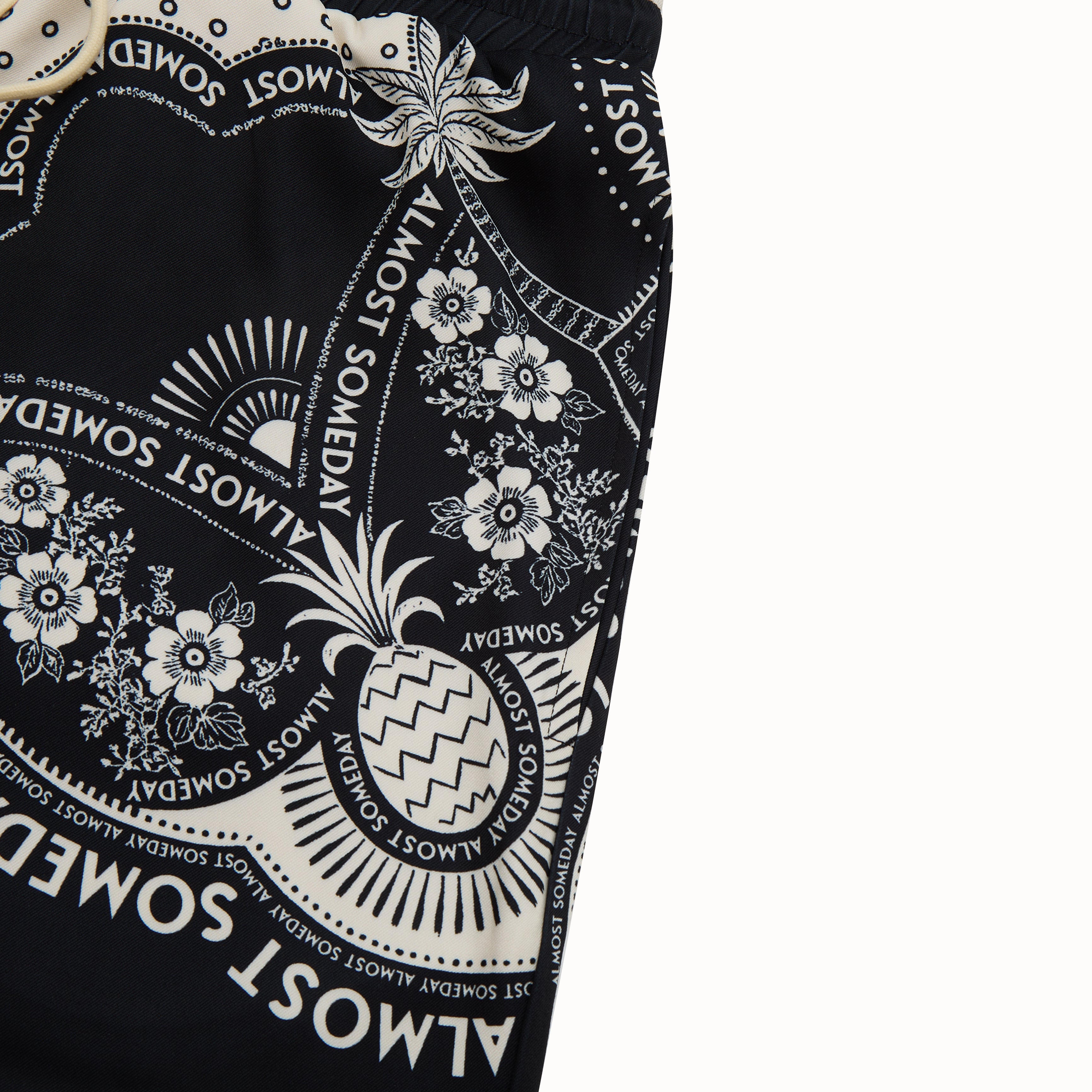 Black shorts with white floral and pineapple pattern on a white background