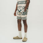A model wearing a beige and navy blue patterned Almost Someday shorts set, including a matching top and shorts, styled with white socks and beige Birkenstock clogs against a plain white studio background.