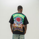 A man viewed from behind wearing a black graphic t-shirt with a large colorful print on the back, paired with light blue jeans, against a plain light gray studio background.