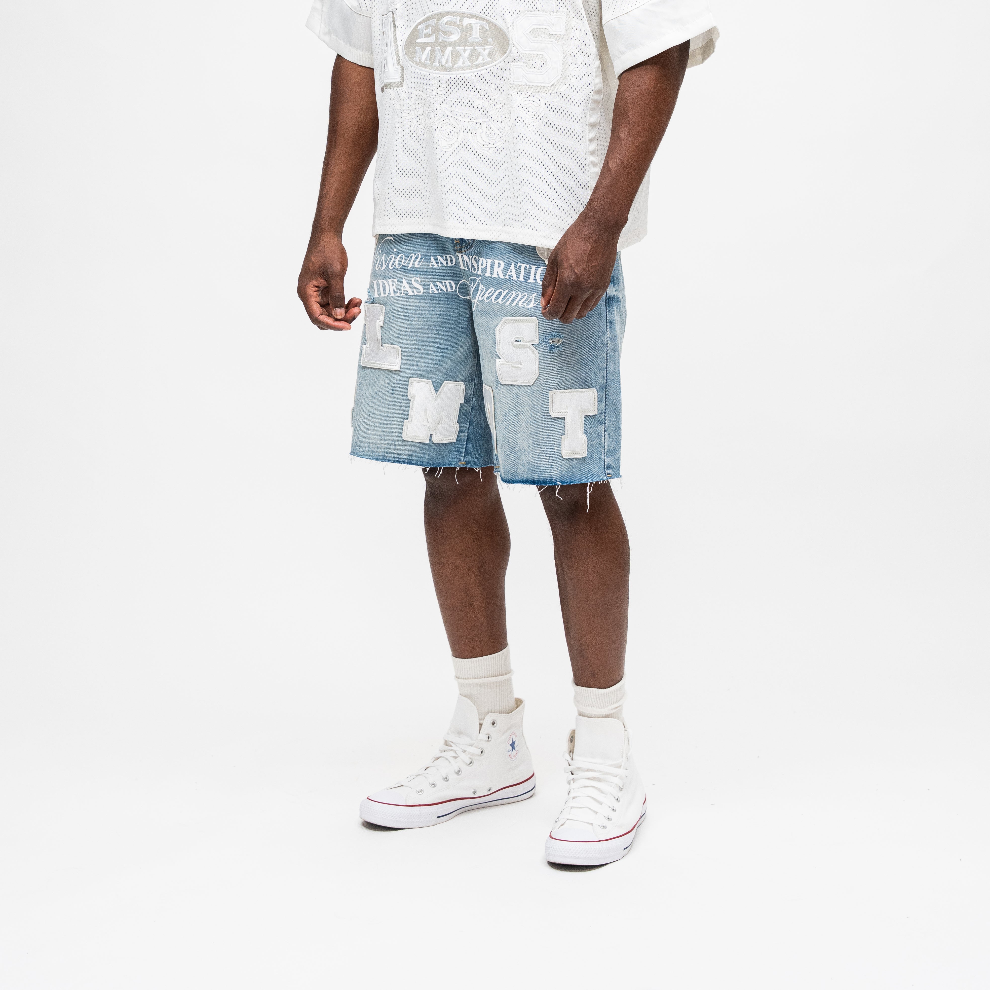 ALMOST SOMEDAY Letterman Denim Jort in Blue Wash, angled front view showing block letter appliqué detail and raw frayed hem

