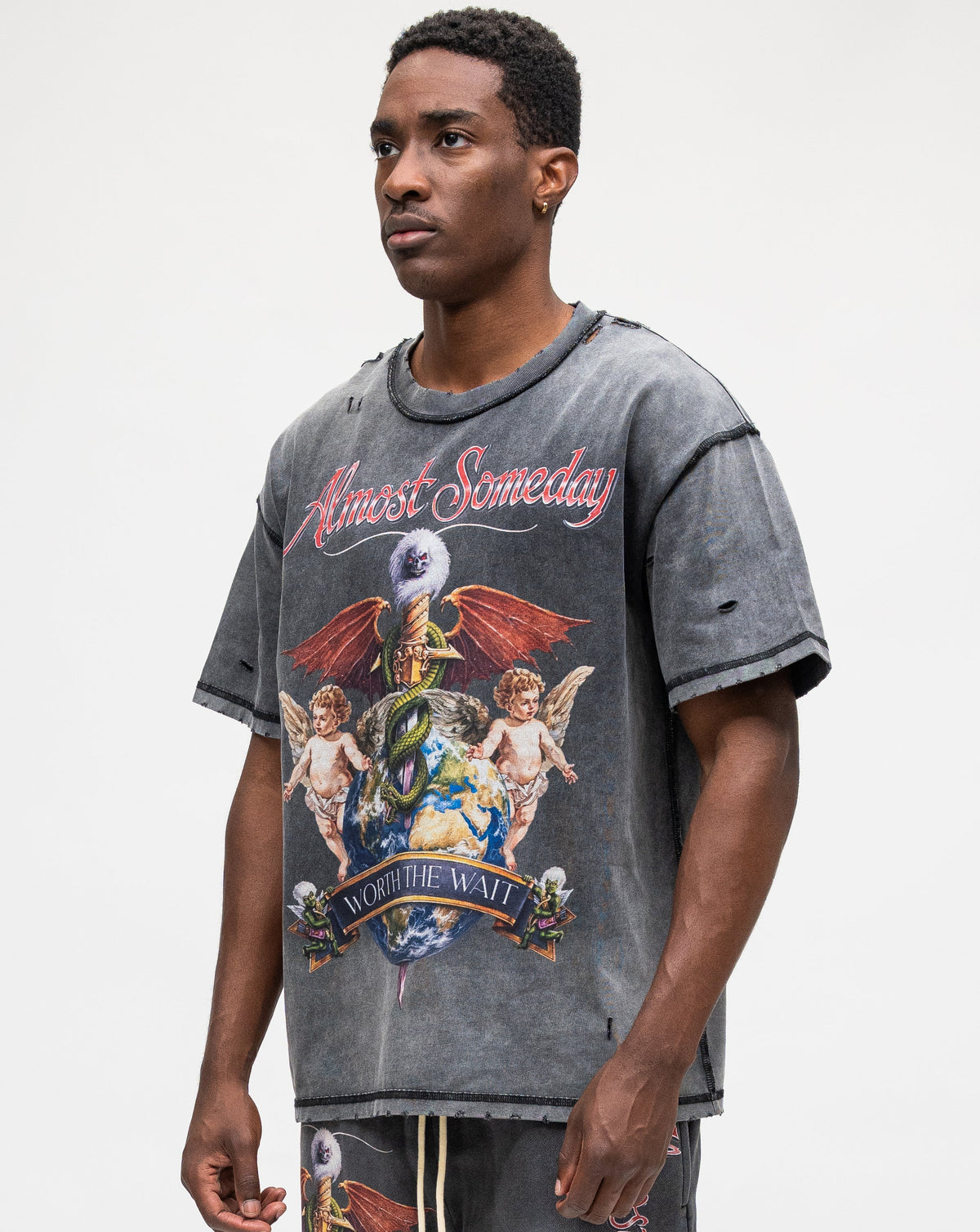A man modeling a washed charcoal gray graphic t-shirt with a 'Anime Someday' cherub design, paired with matching graphic sweatpants, against a plain light gray background.