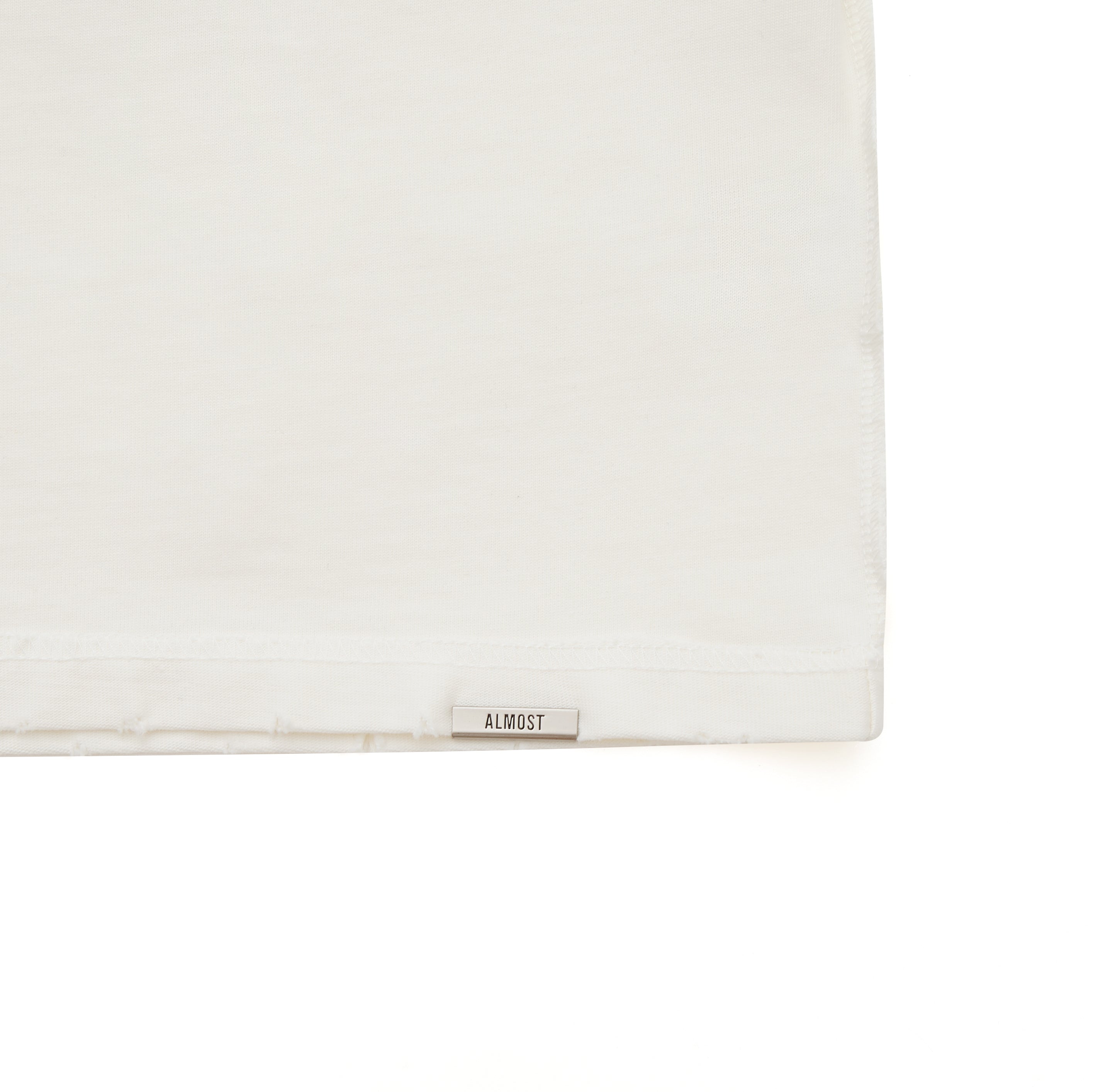 Cream tshirt with a small rectangular object labeled 'ALMOST' on a white background