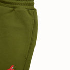 Close-up of olive green sweatpants with a red logo on a white background