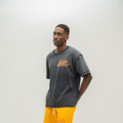A man wearing a washed black t-shirt with a yellow and red graphic on the chest, paired with bright yellow sweatshorts, standing against a light gray studio background.