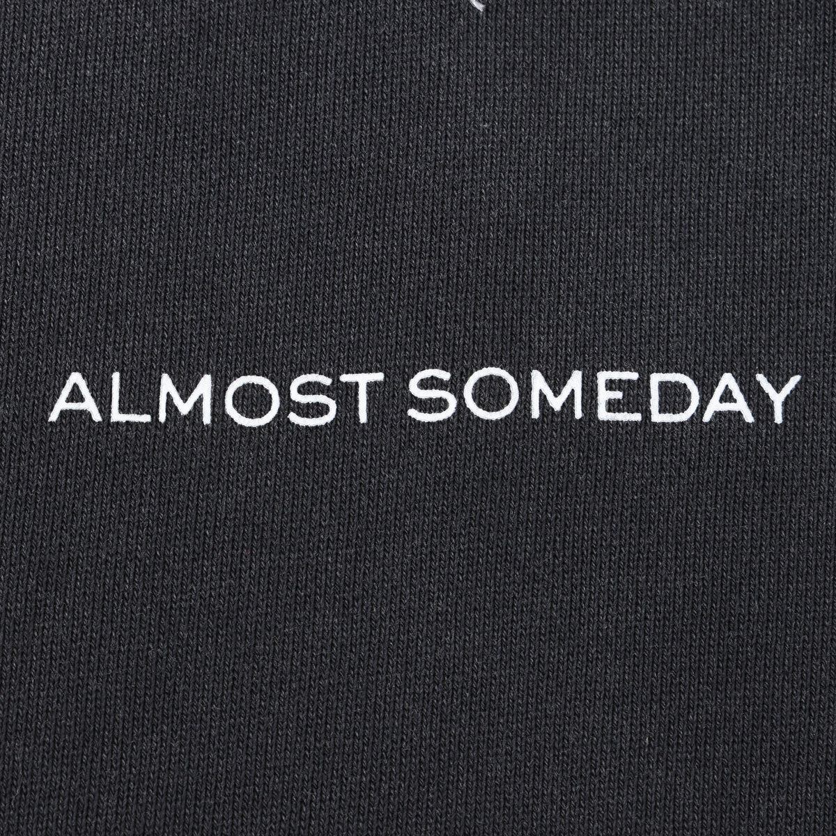 Alumni Crewneck – Black – Close-up of white Almost Someday chest lettering on black knit fabric