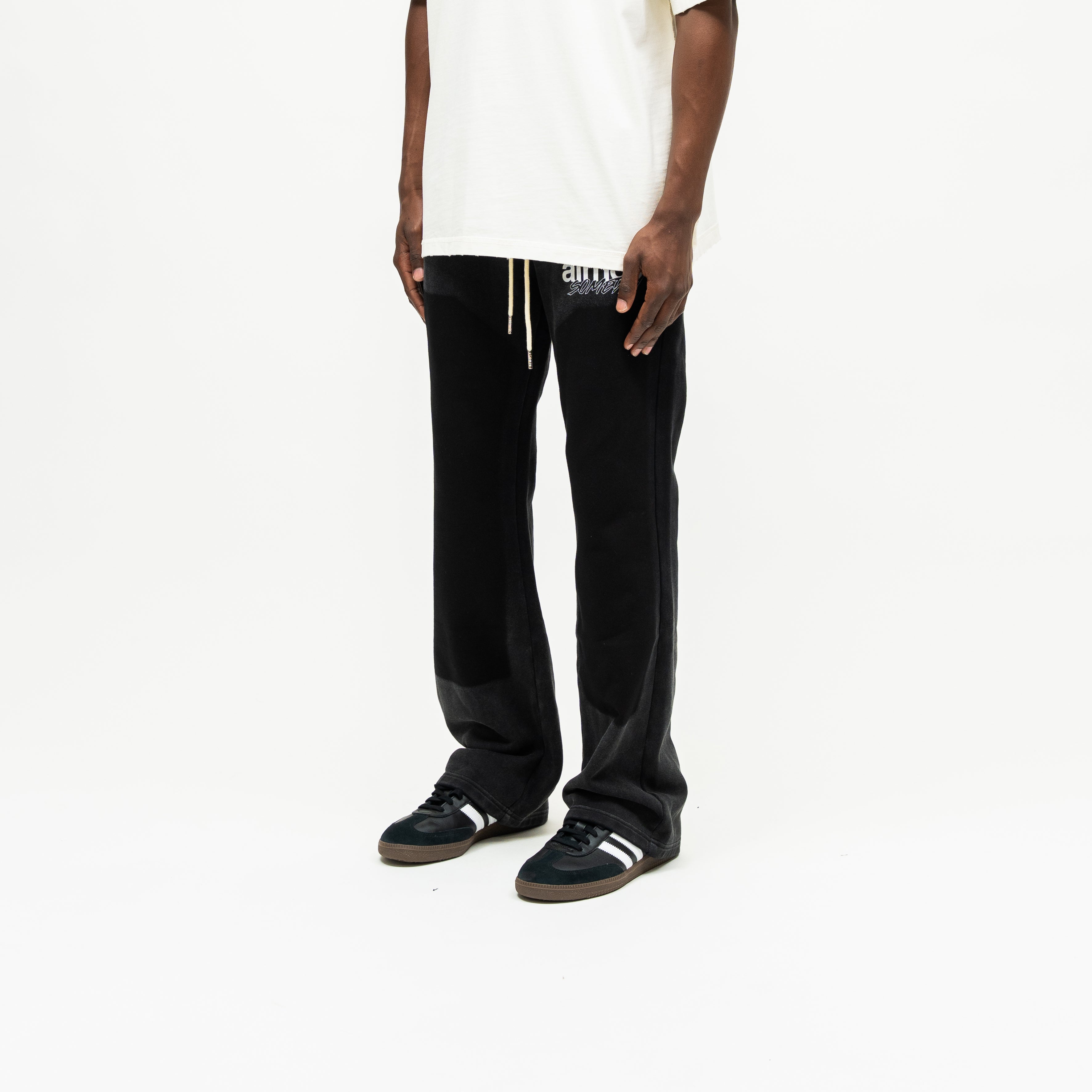 Enemies Flare Bottoms – Black – Three-quarter front view on model styled with a cream tee, showing white thigh logo and flared hems
