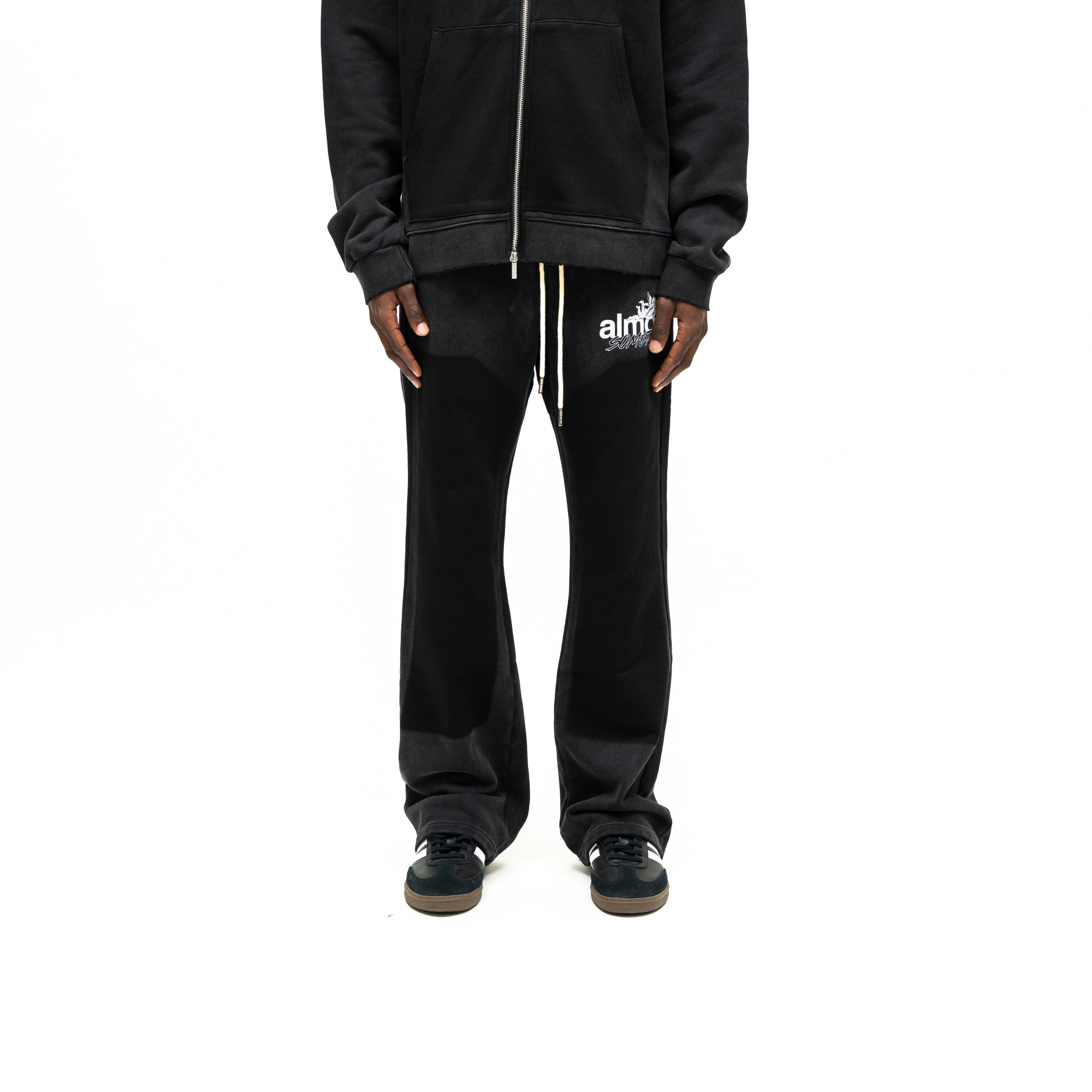 Enemies Flare Bottoms – Black – Front view on model styled with a black zip hoodie, showing white drawstrings and thigh logo