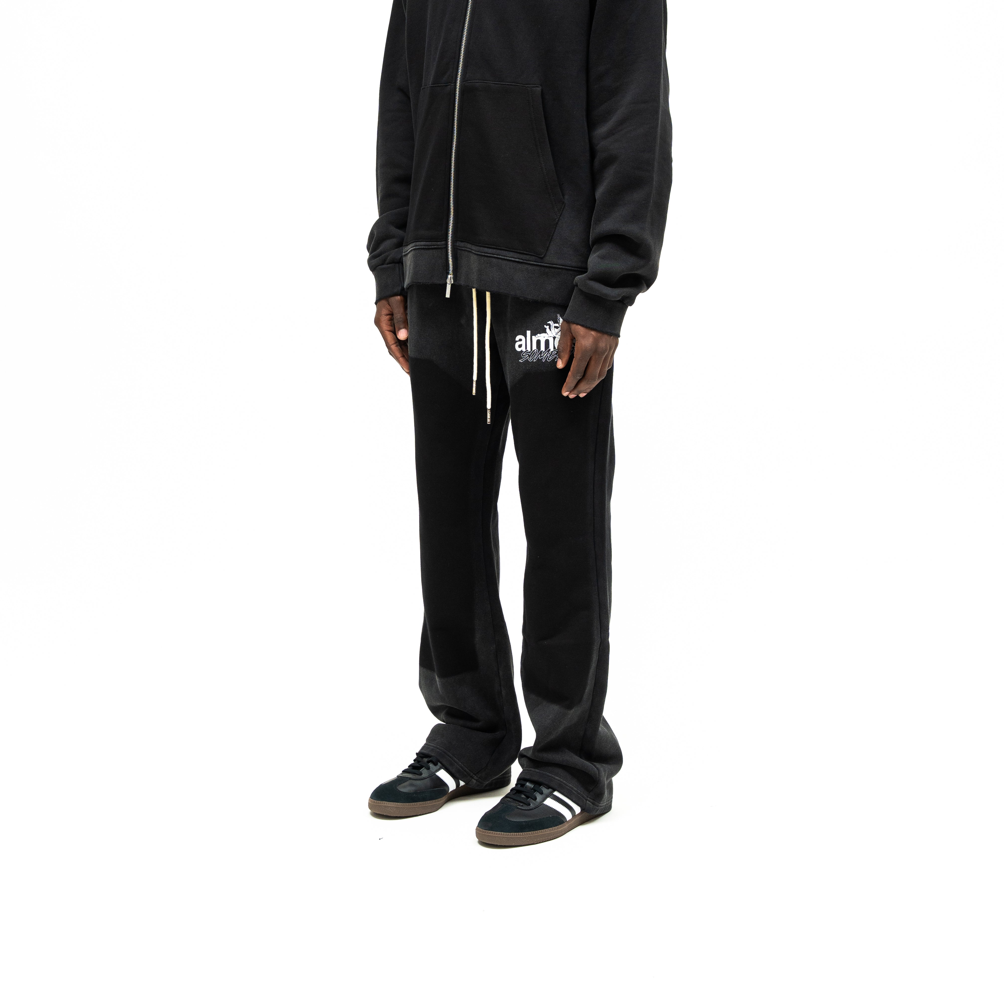 Enemies Flare Bottoms – Black – Three-quarter front view on model styled with a black zip hoodie, showing thigh logo and flared hems
