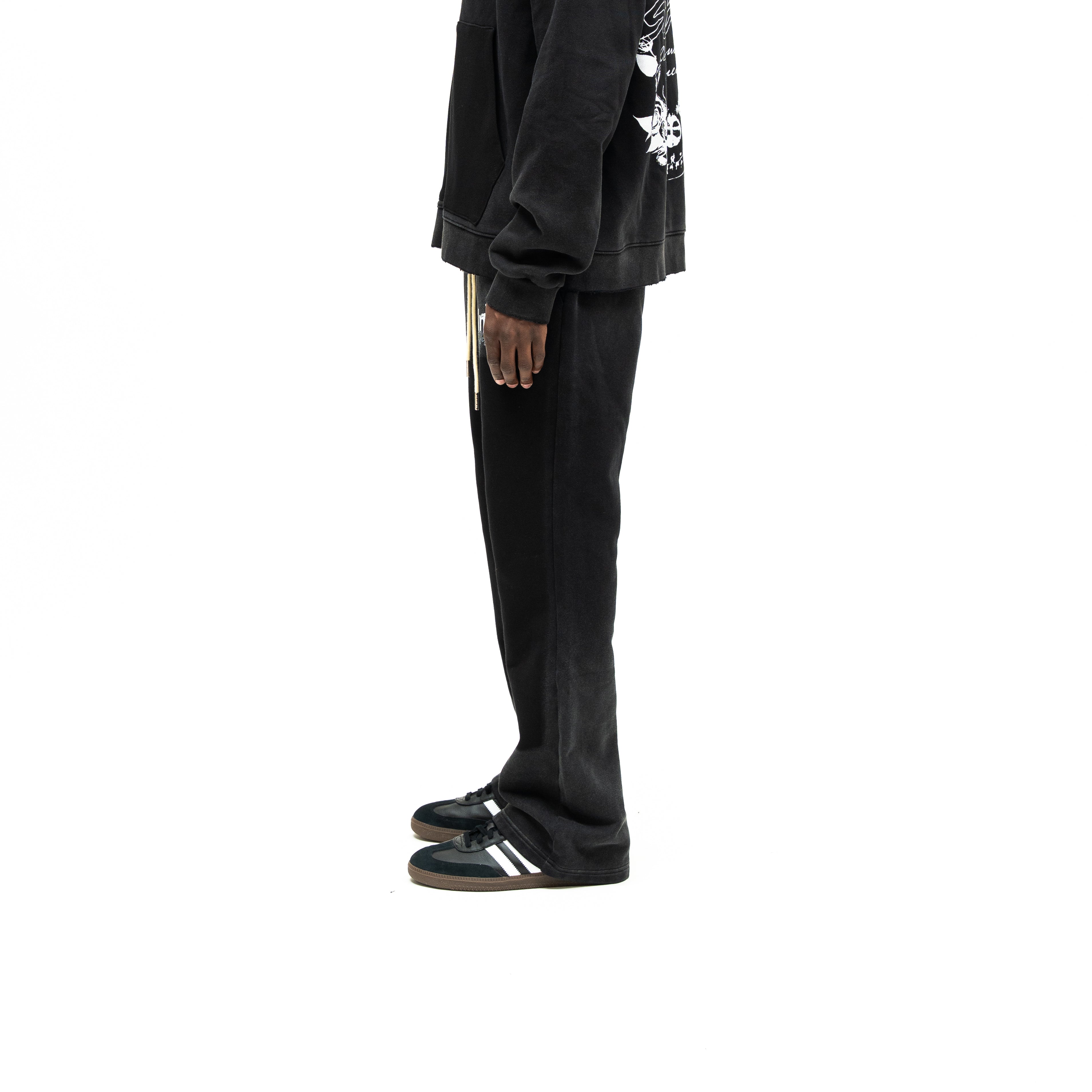 Enemies Flare Bottoms – Black – Side view on model styled with a black zip hoodie, showing leg silhouette and flared hem