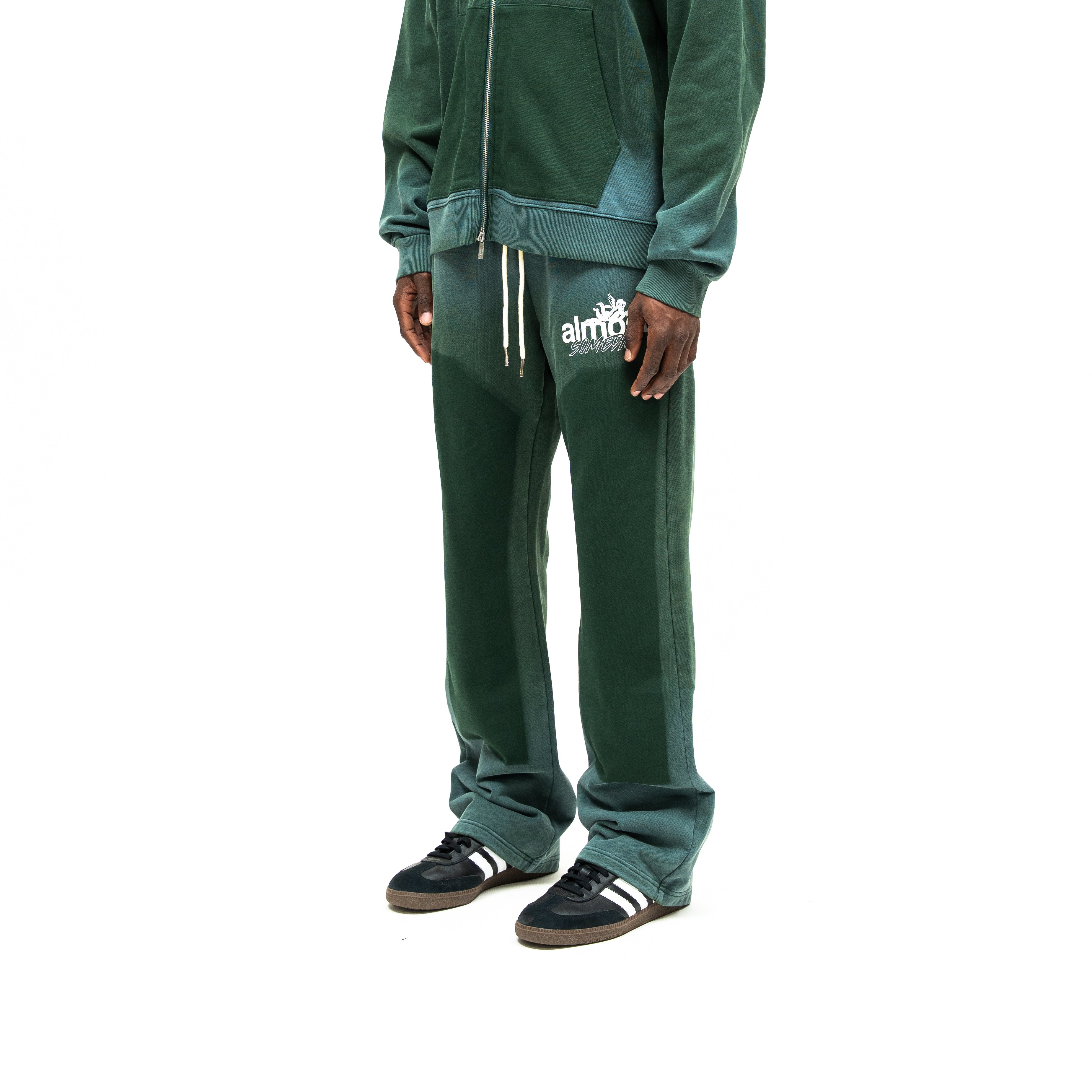 Enemies Flare Bottoms – Green – Three-quarter front view on model styled with a matching zip hoodie, showing white thigh logo and dark leg panels