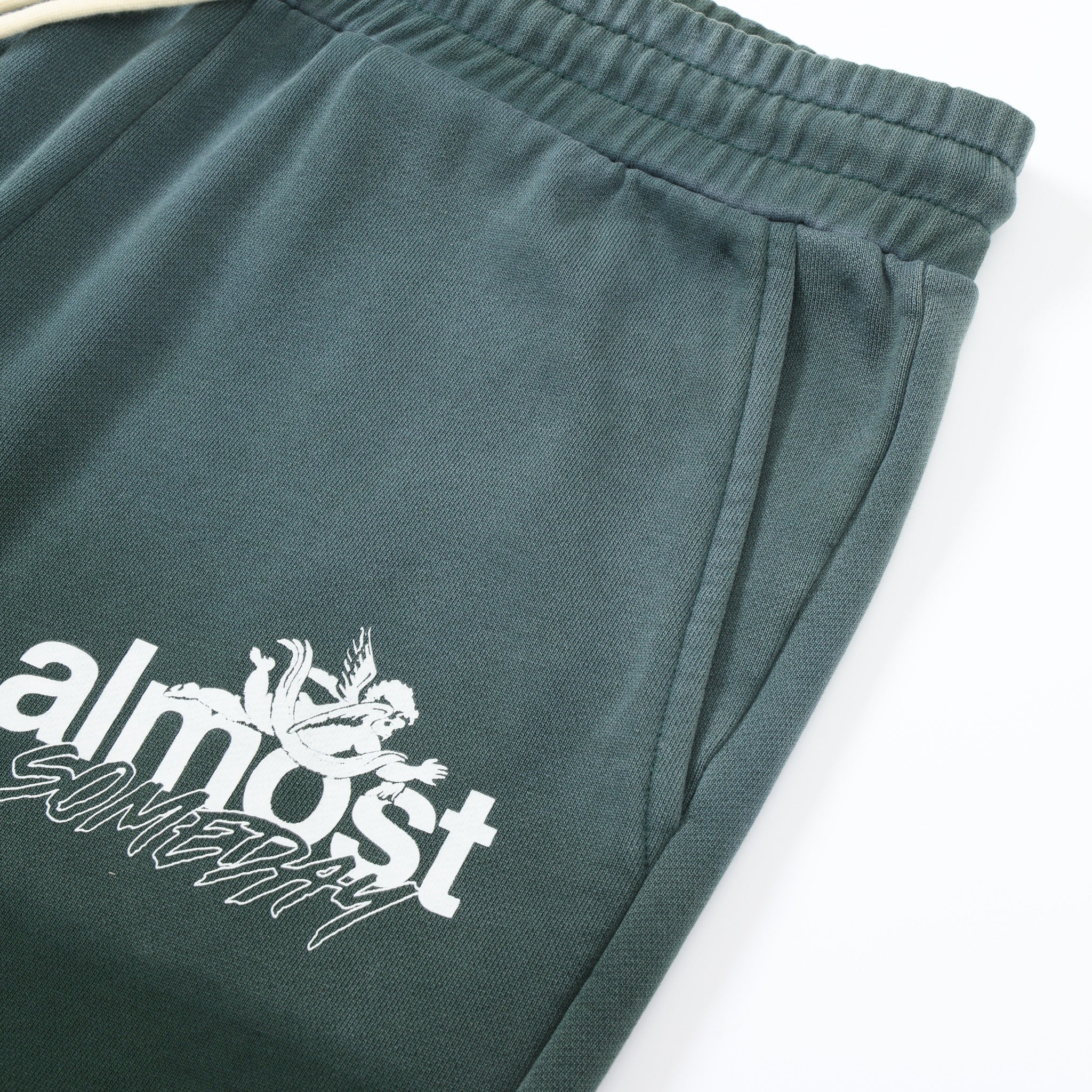 Enemies Flare Bottoms – Green – Close-up of angled front pocket, elastic waistband, and white logo