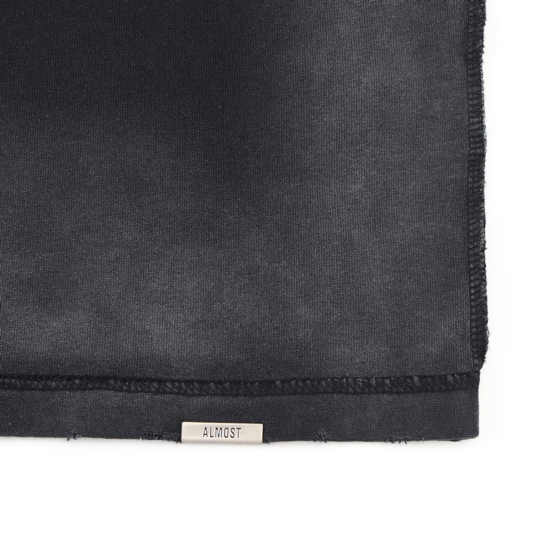 Enemies Tee – Black – Close-up of bottom hem with metal ALMOST logo tab