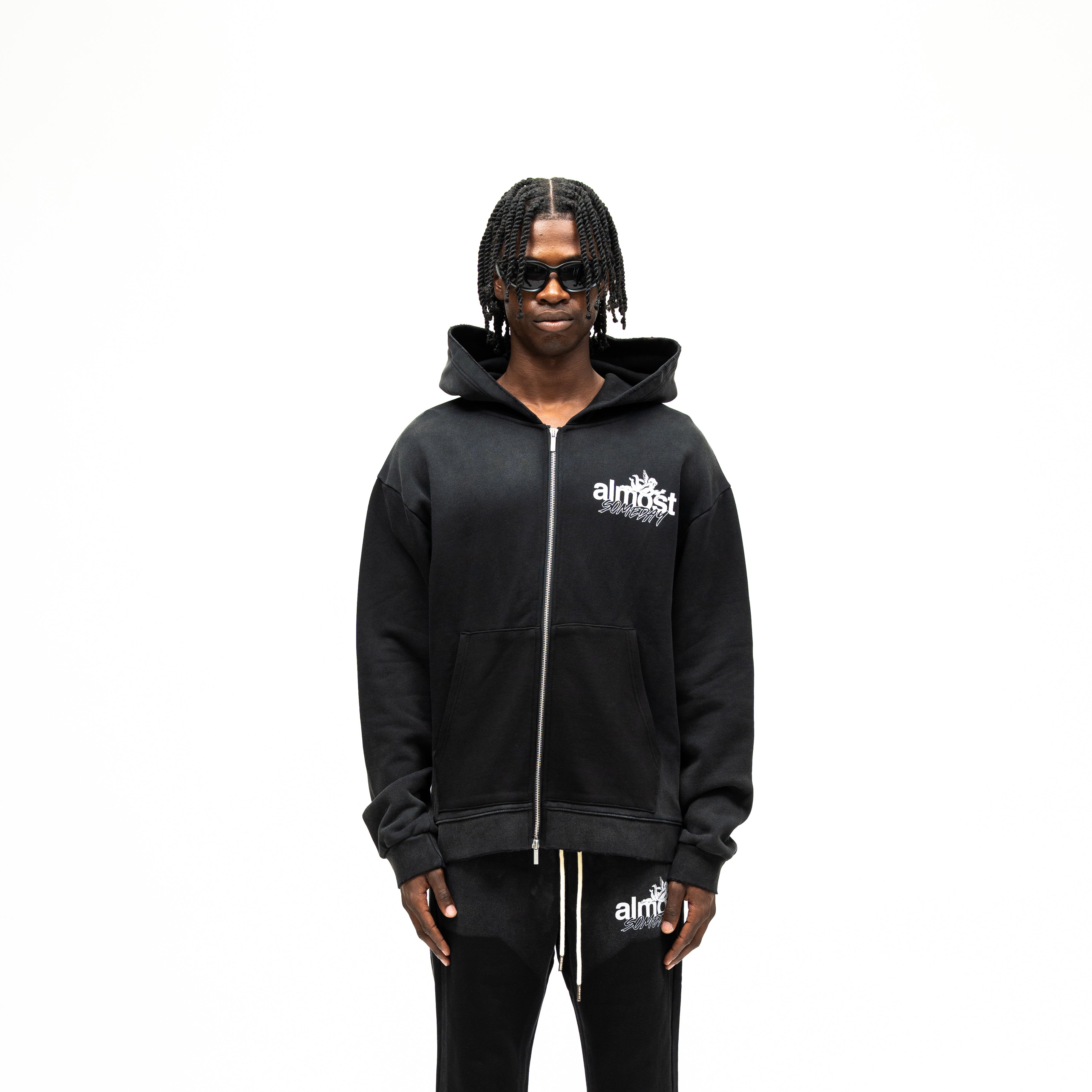 Enemies Zip Hoodie – Black – Front view on model showing full zipper, white chest logo, hood, and front pocket detail