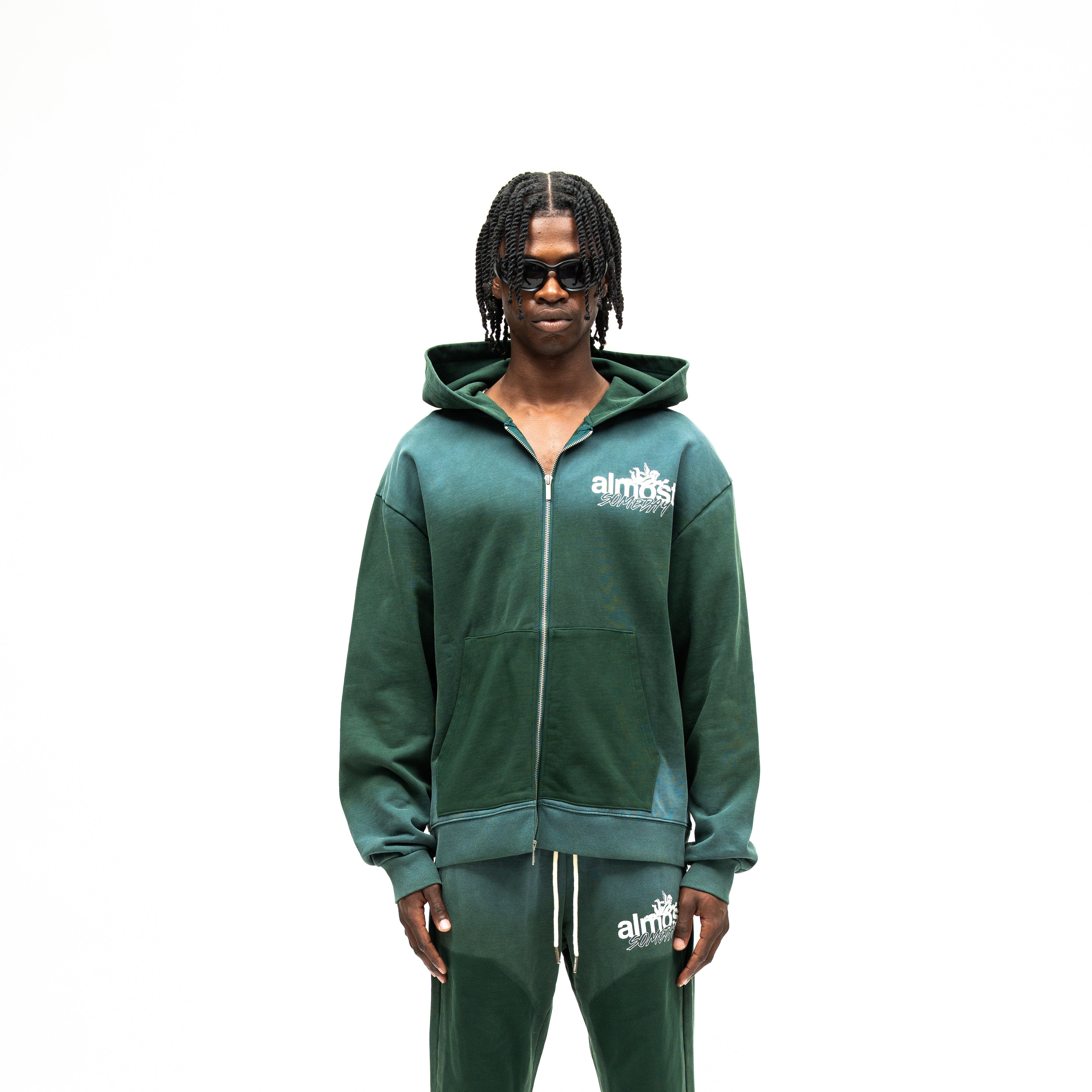 Enemies Zip Hoodie – Green – Front view on model showing full zipper, white chest logo, hood, and dark green front pockets
