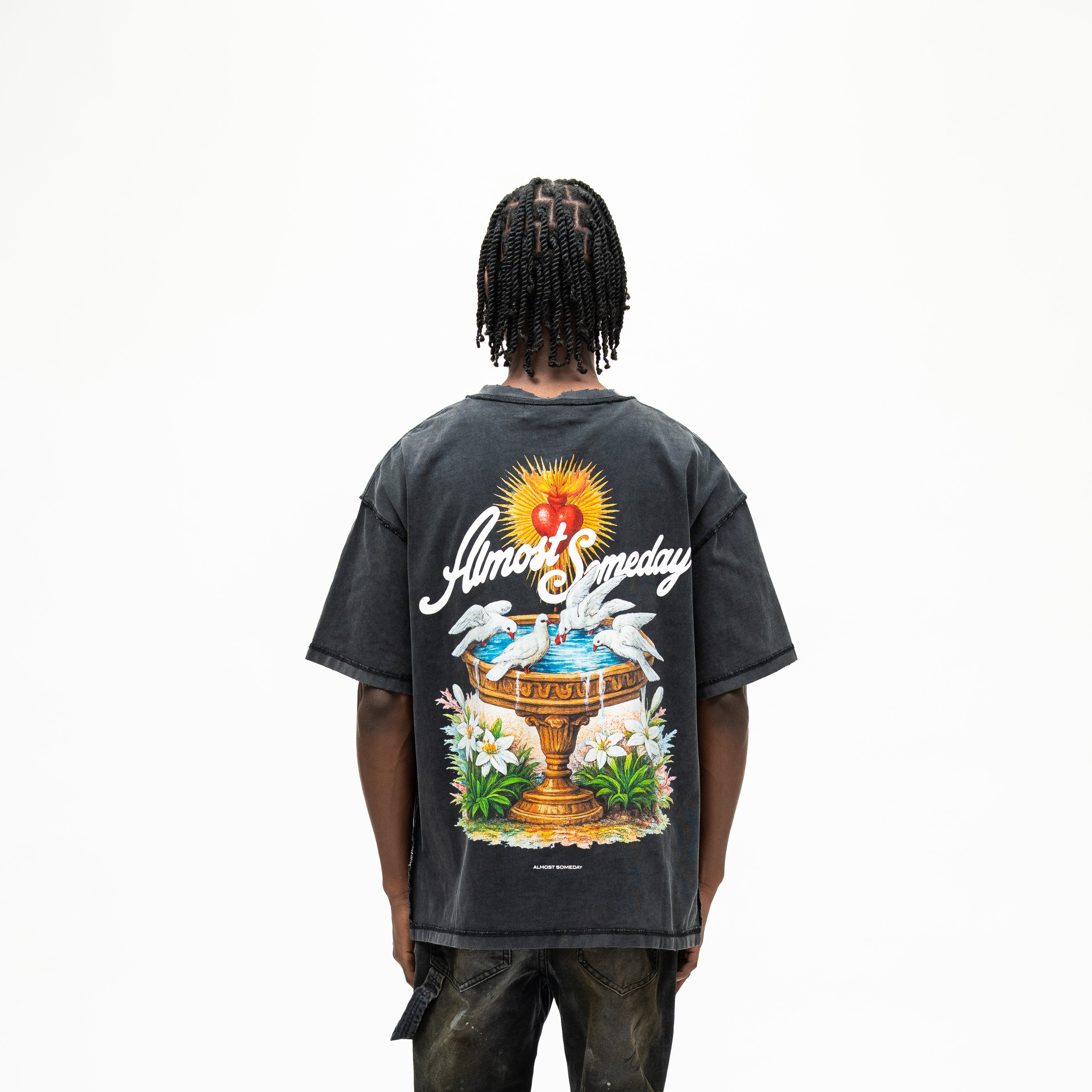 Fountain Tee – Black – Back view on model showing fountain, white doves, flowers, red heart, and ALMOST SOMEDAY lettering